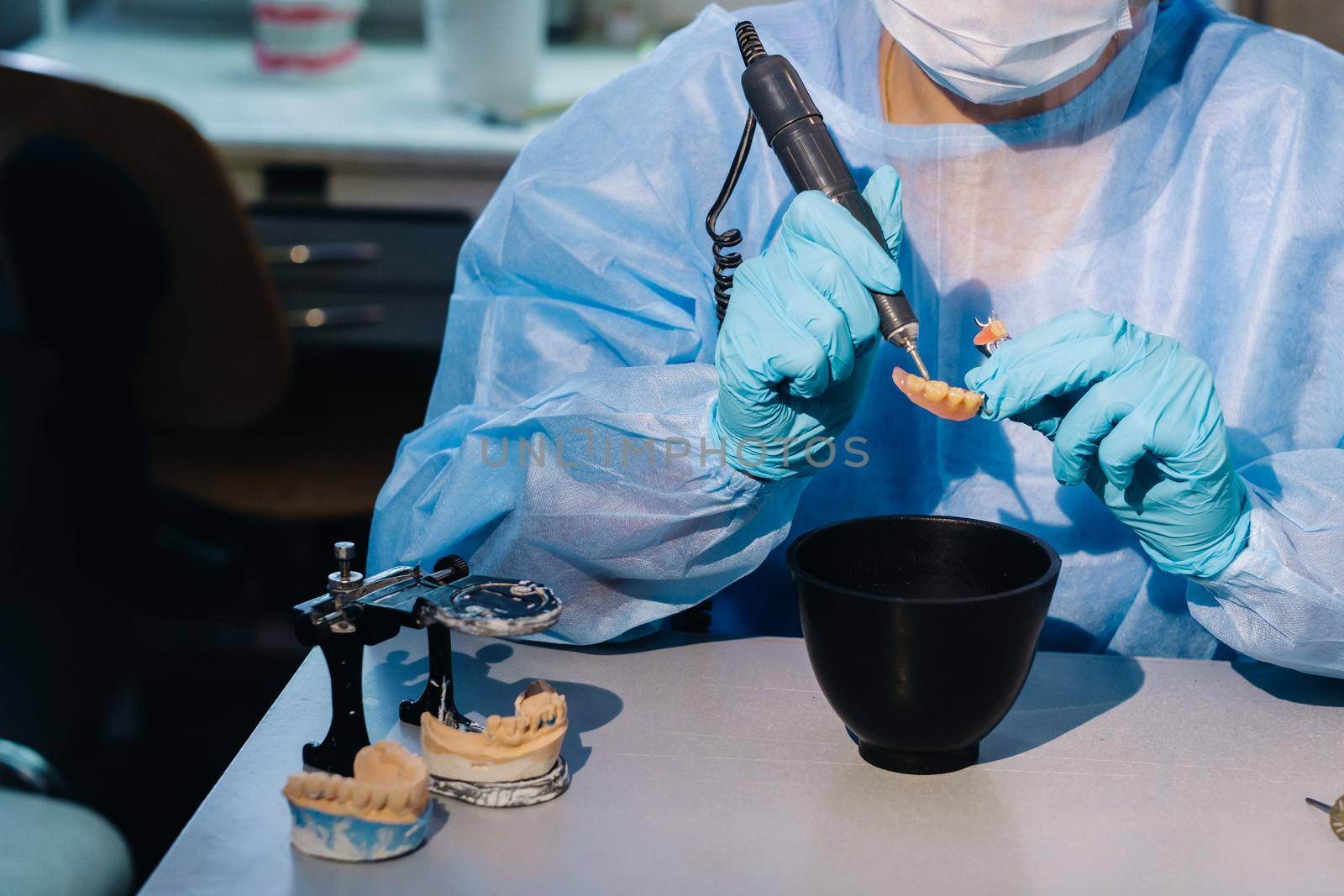 A masked and gloved dental technician works on a prosthetic tooth in his lab by Lobachad