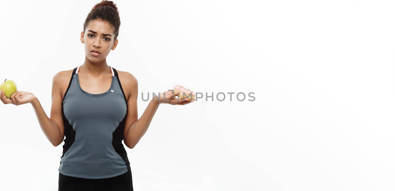 Healthy and diet concept - Beautiful sporty African American make a decision between donut and green apple. Isolated on white background