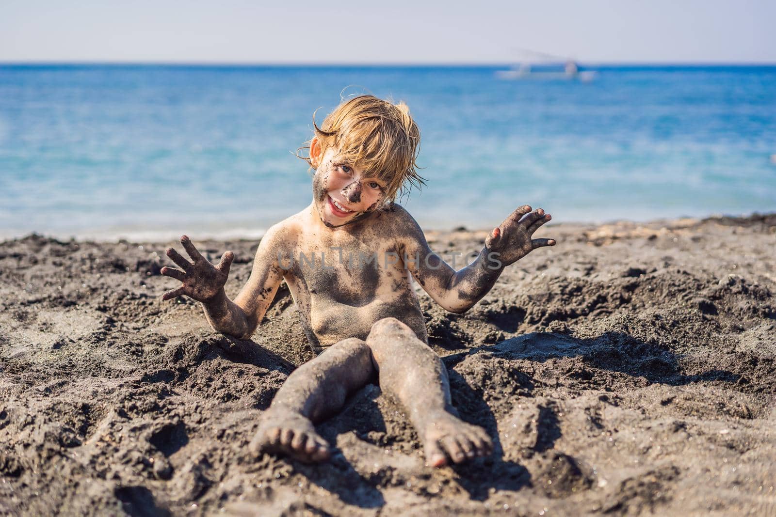 Black Friday concept. Smiling boy with dirty Black face sitting and playing on black sand sea beach before swimming in ocean. Family active lifestyle, and water leisure on summer vacation with kids. Black Friday, sales of tours and airline tickets or goods by galitskaya