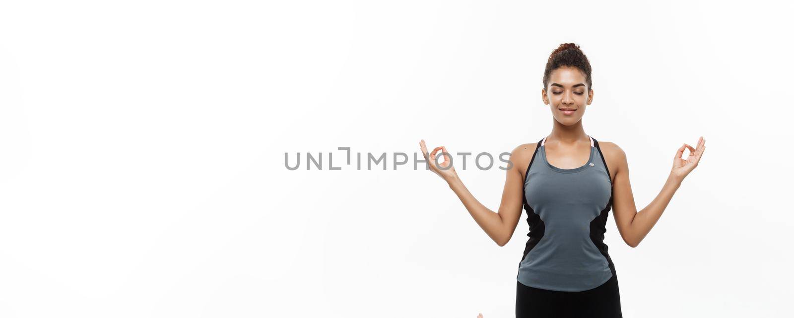 Healthy and Fitness concept - Beautiful American African lady in fitness clothing doing yoga and meditation. Isolated on white background. by Benzoix