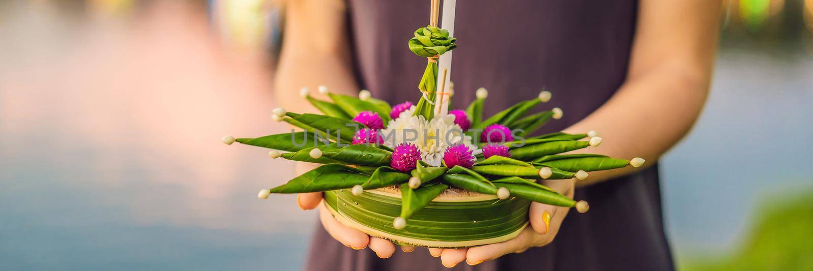 BANNER, LONG FORMAT A female tourist holds the Loy Krathong in her hands and is about to launch it into the water. Loy Krathong festival, People buy flowers and candle to light and float on water to celebrate the Loy Krathong festival in Thailand by galitskaya