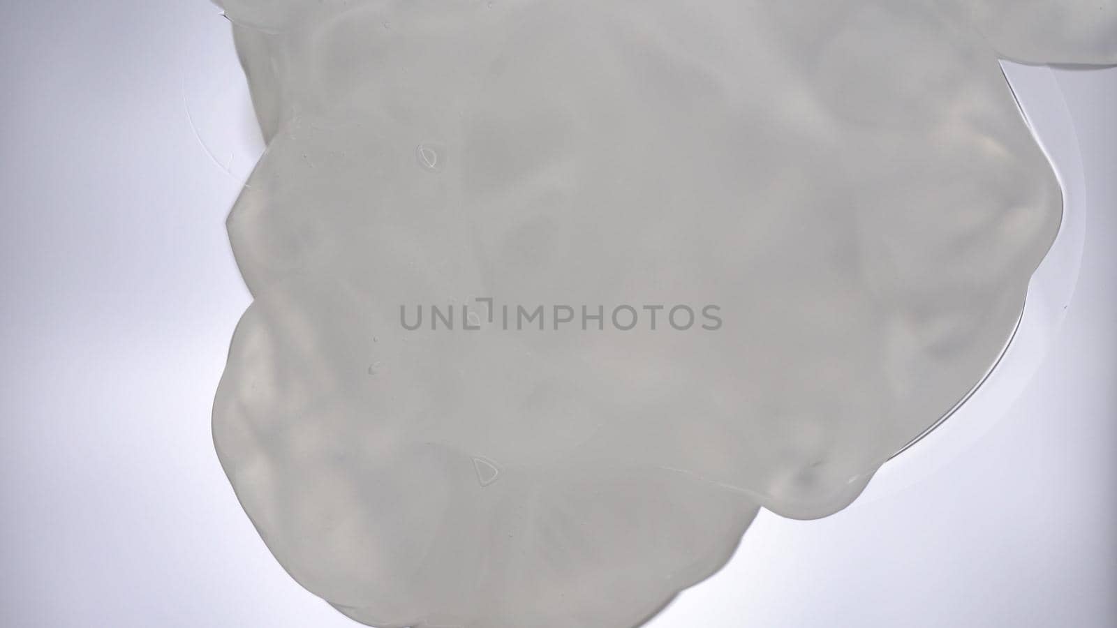 A drop of shampoo falls on the glass on a bright white background. Macro bottom view on the shampoo. 4k