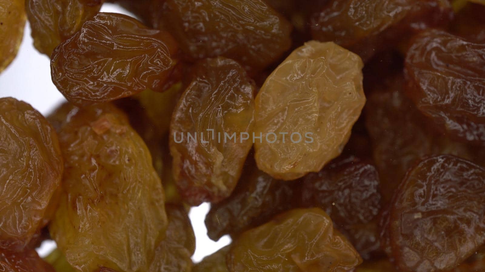 Raisins fall on glass on a bright white background. Raisins macro bottom view. 4k