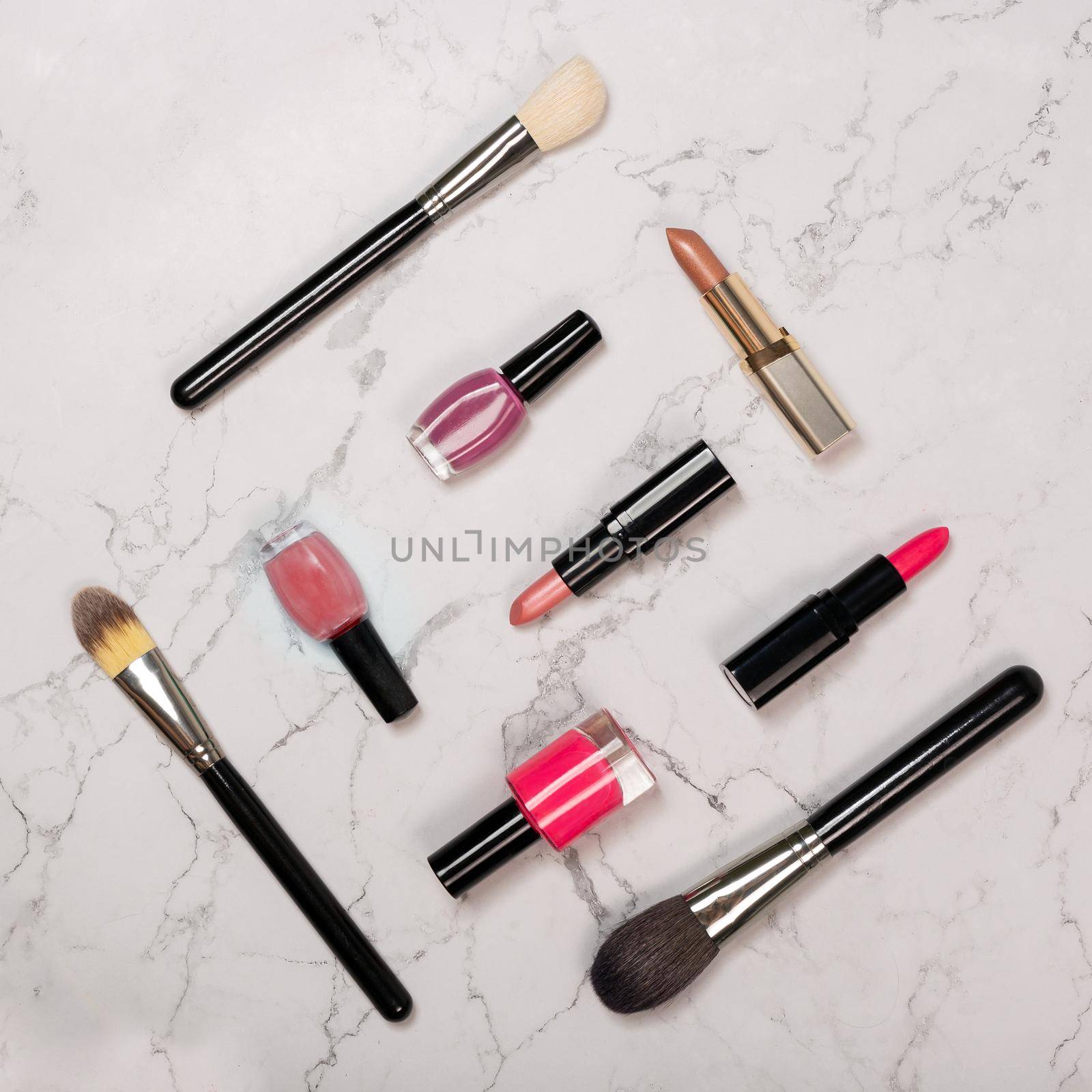 Flat lay of cosmetic products including lipsticks, nail varnish, makeup brushes on white marble background