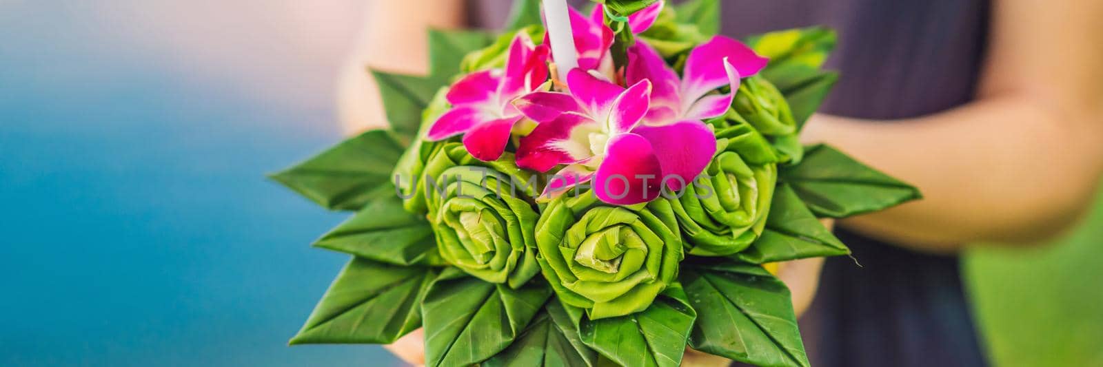 BANNER, LONG FORMAT A female tourist holds the Loy Krathong in her hands and is about to launch it into the water. Loy Krathong festival, People buy flowers and candle to light and float on water to celebrate the Loy Krathong festival in Thailand by galitskaya