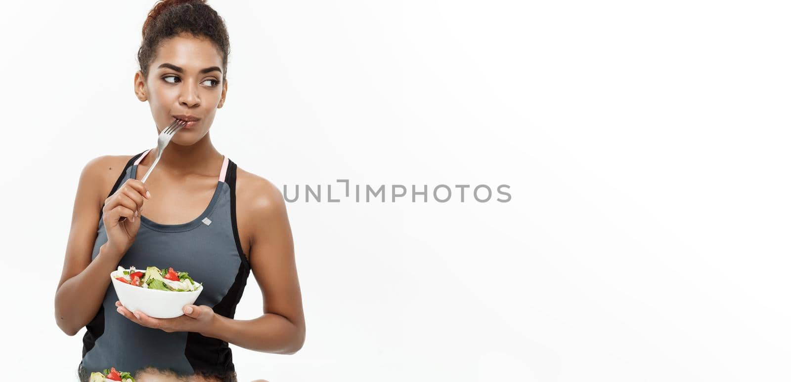 Healthy and Fitness concept - Beautiful American African lady in fitness clothes on diet eating fresh salad. Isolated on white background