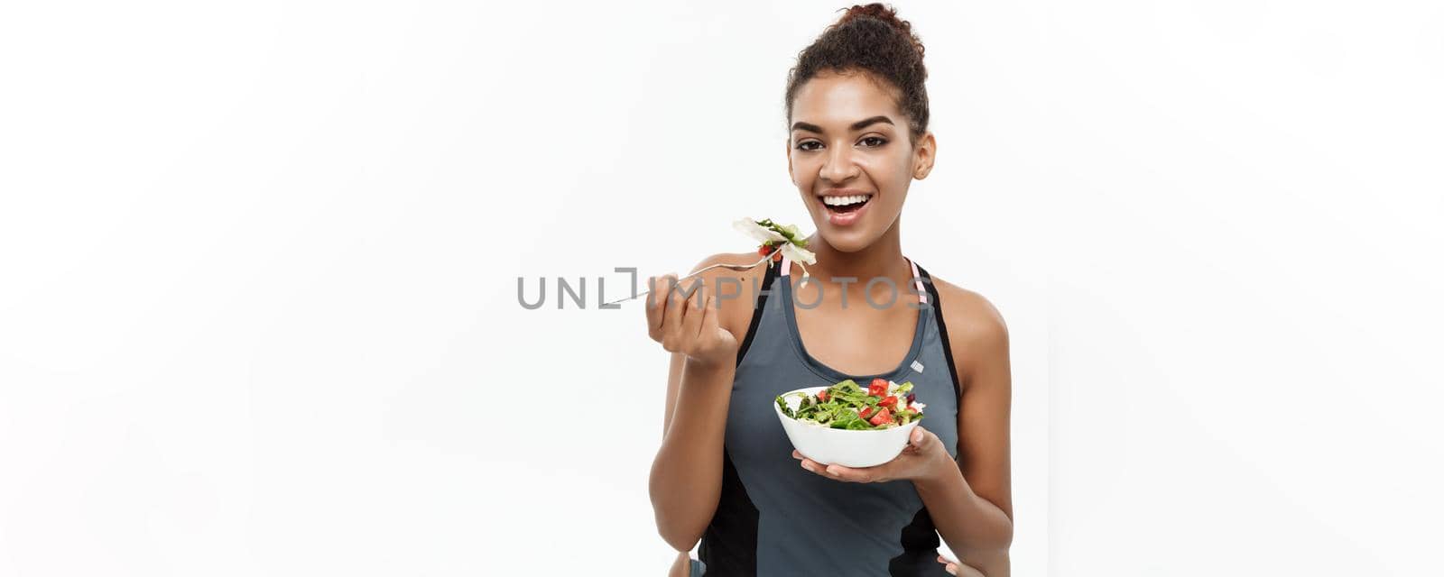Healthy and Fitness concept - Beautiful American African lady in fitness clothes on diet eating fresh salad. Isolated on white background