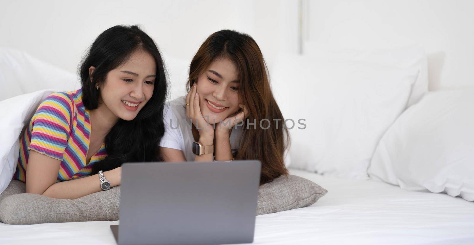 Young asian LGBT Lesbian couples are using laptops to search for information to buy a new home. while embracing each other in bed..