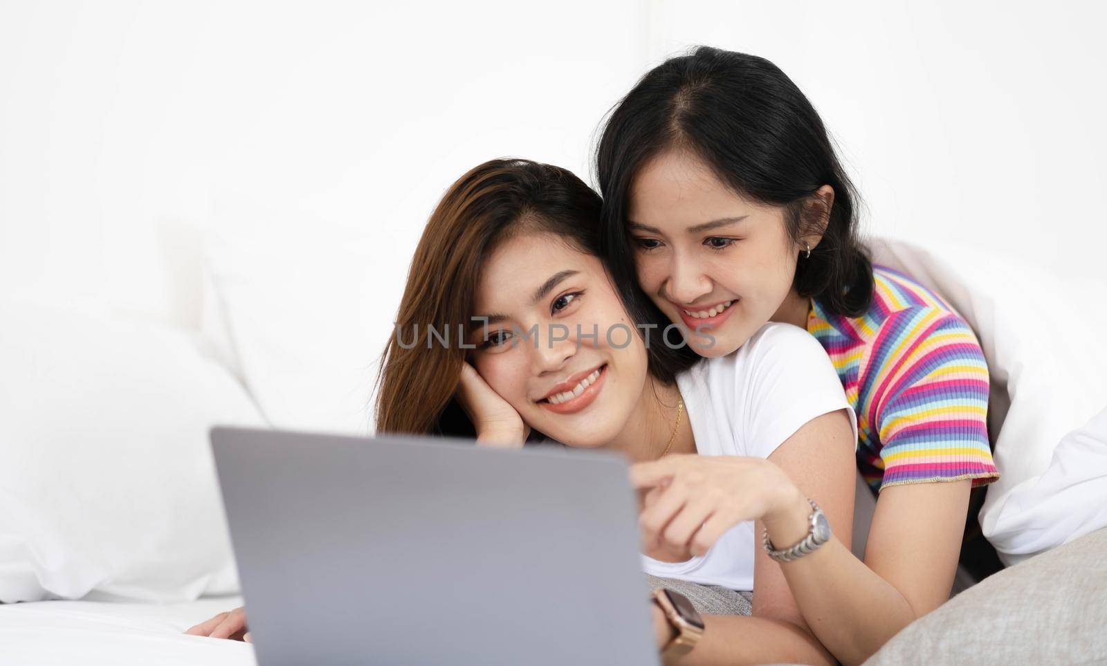 A couple of lovely woman listening song and watch movie with laptop in bed while smiling. They are happiness and building good relationships in the future. by wichayada