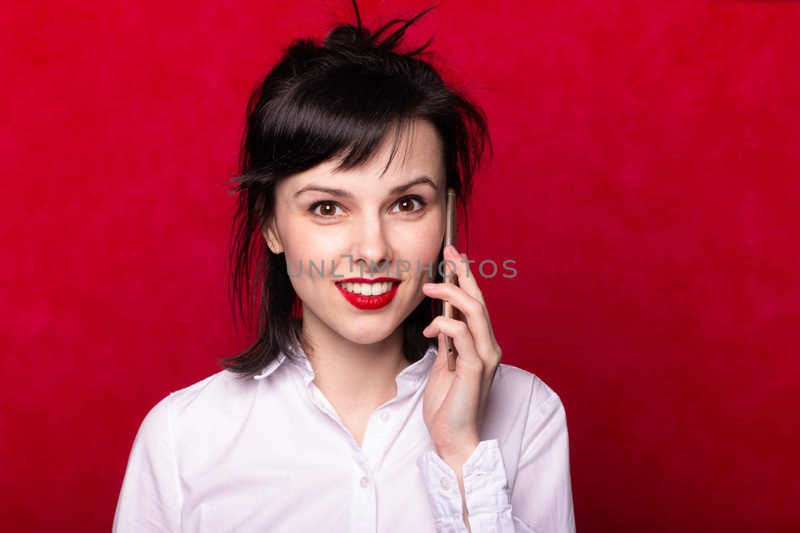 beautiful woman manager in a white shirt speaks on the phone, red lips, red background. High quality photo