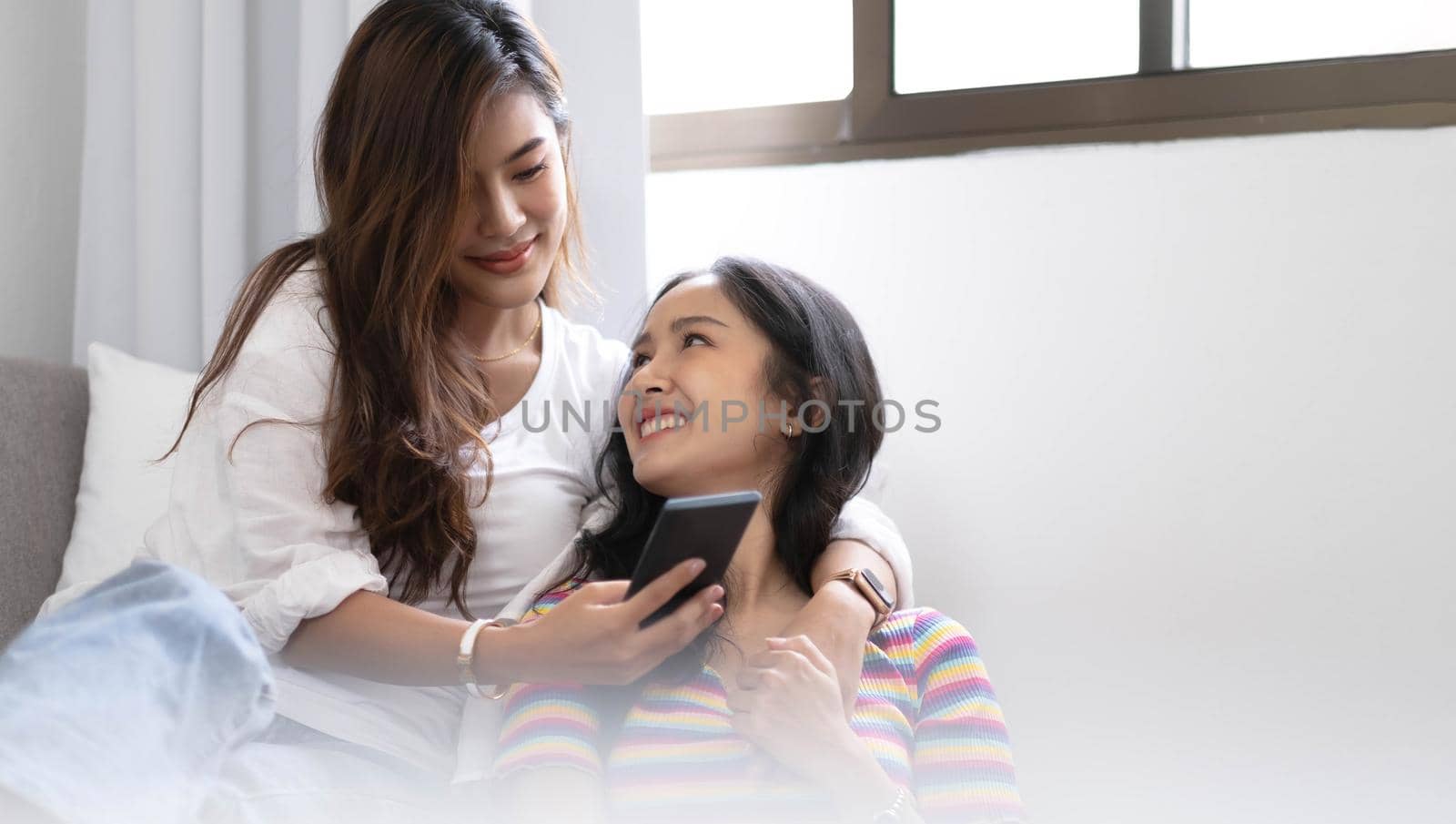 Young beautiful Asian women lesbian couple lover using smartphone video call online in living room on sofa at home with smiling face.Concept of LGBT sexuality with happy lifestyle together. by wichayada