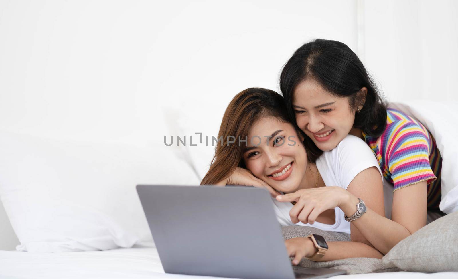 A couple of lovely woman listening song and watch movie with laptop in bed while smiling. They are happiness and building good relationships in the future. by wichayada