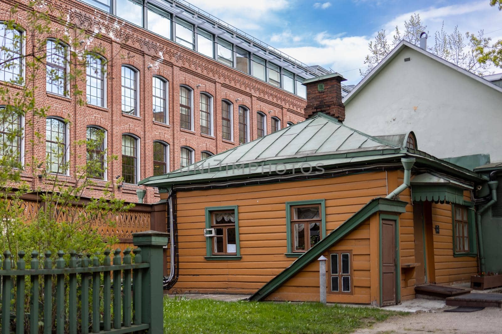 An old wooden manor house on the background of a modern office building made of red brick. A clear sunny day with a blue sky with clouds. High quality photo
