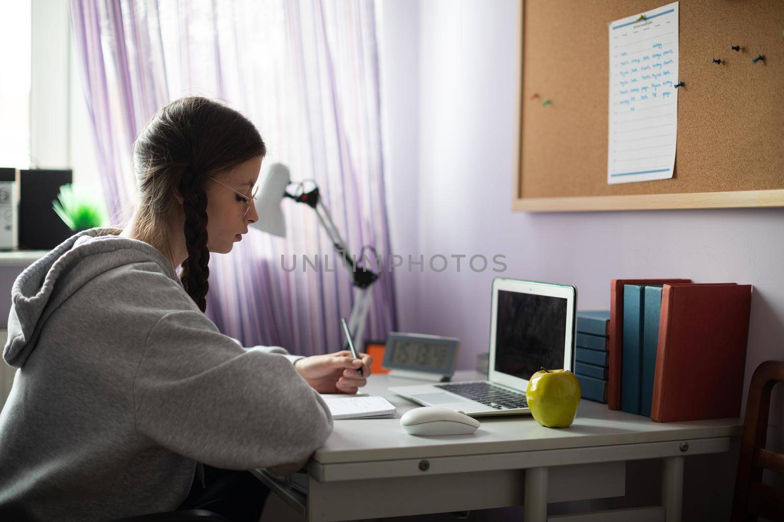 At home in her room, the teenager sits at her desk and solves assignments from school. A diligent student. Remote learning at home.