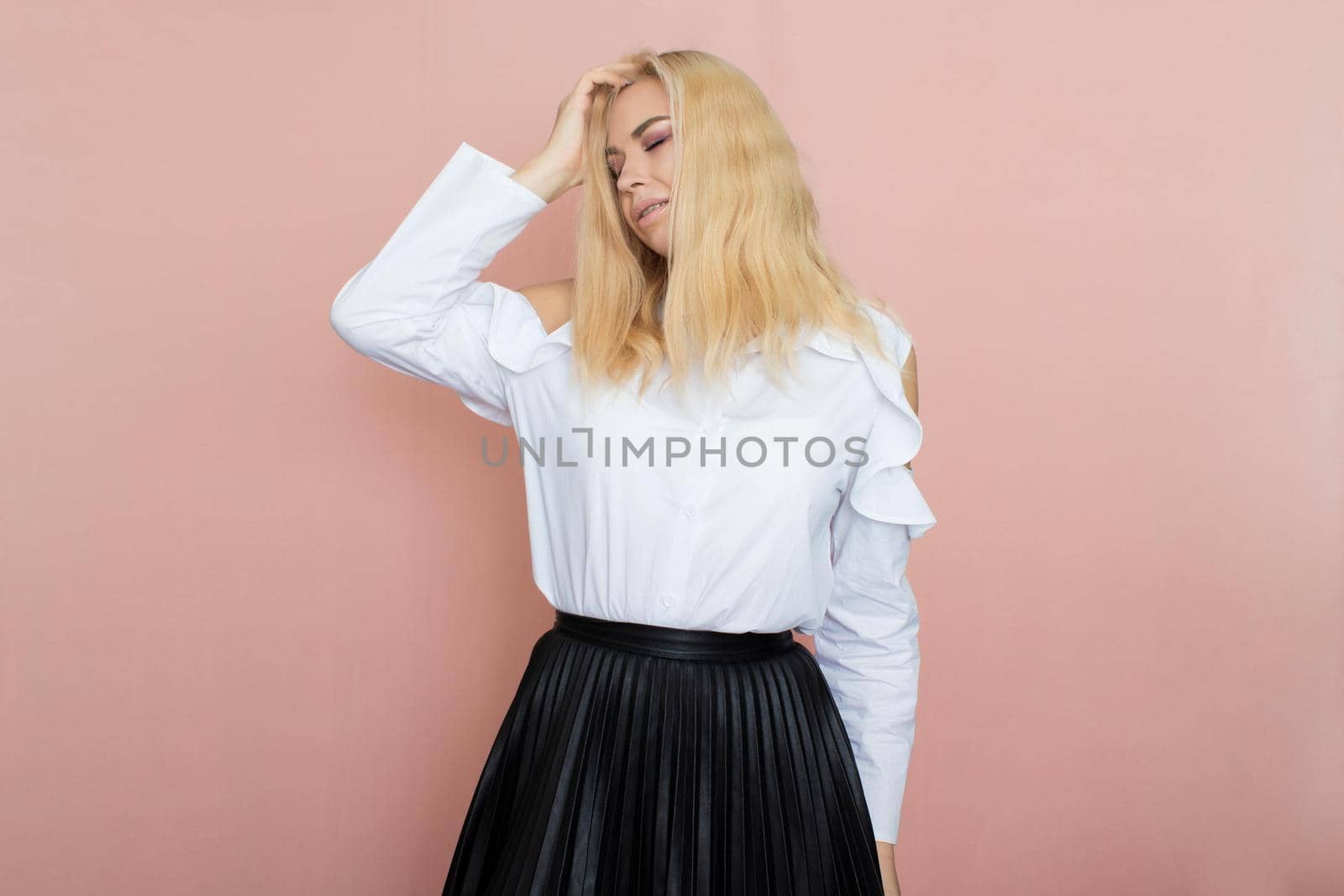 Beauty, fashion portrait. Elegant business style. Portrait of a beautiful blonde woman in white blouse and black skirt posing at studio on a pink background.