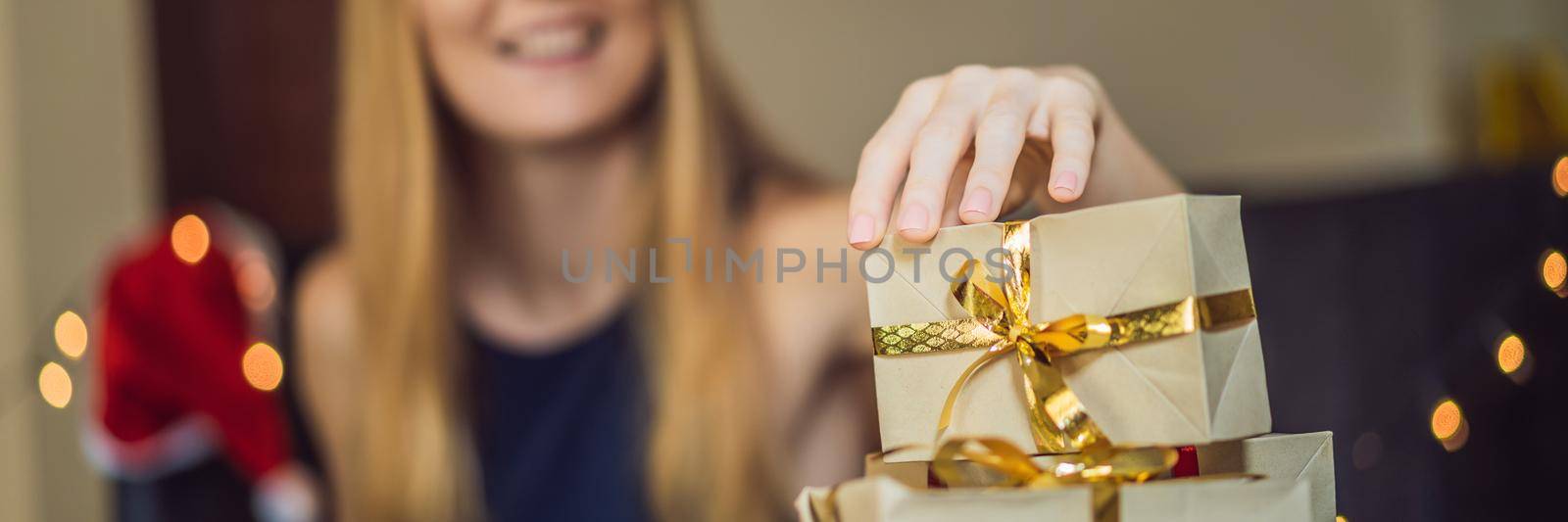 Young woman is packing presents. Present wrapped in craft paper with a red and gold ribbon for christmas or new year. Woman makes an advent calendar for her child. BANNER, LONG FORMAT