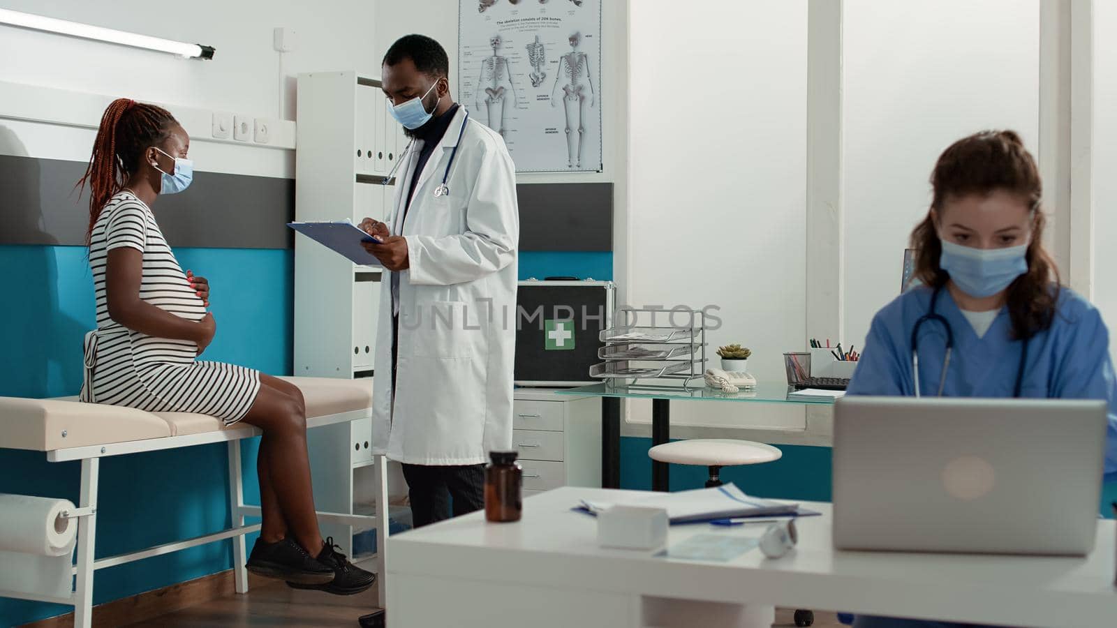 Pregnant woman and physician with face mask doing consultation in health care office. Person expecting child attending checkup appointment with general practitioner at maternity clinic.