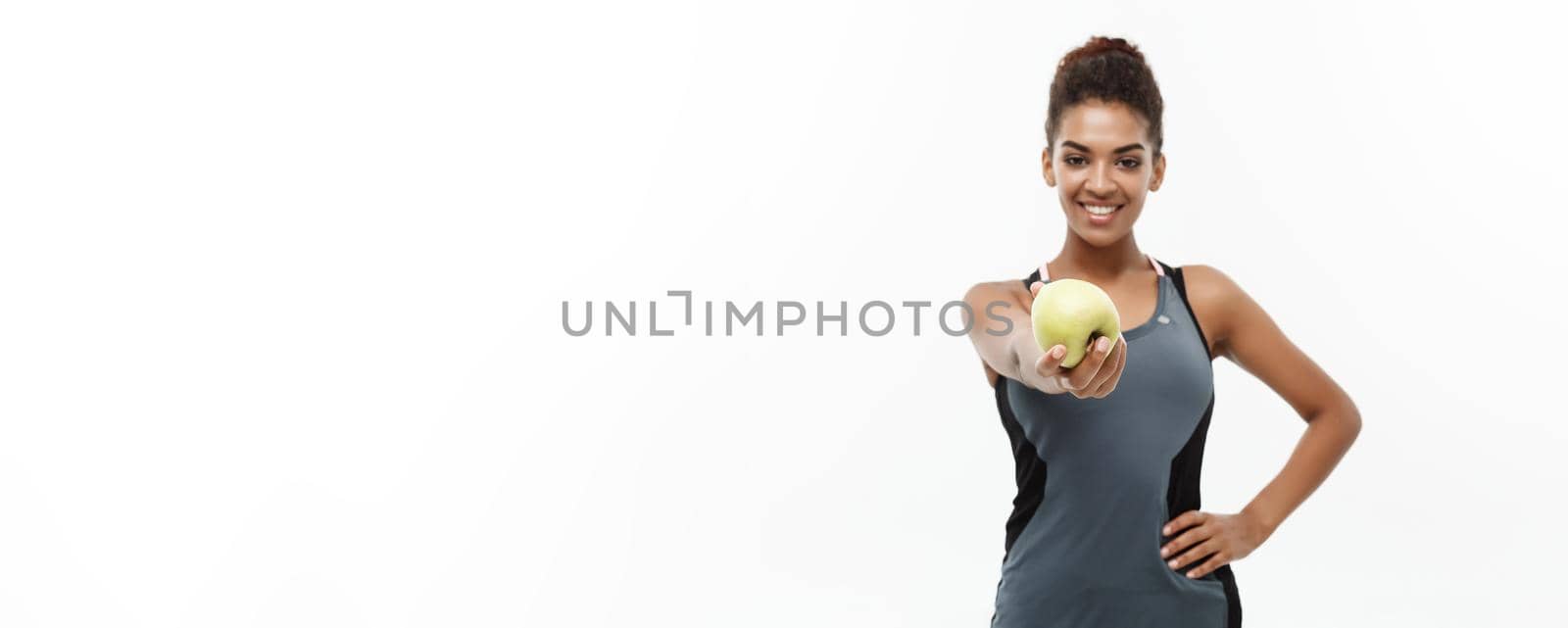 Healthy and Fitness concept - Beautiful American African lady in grey fitness clothes holding green apple. Isolated on white background