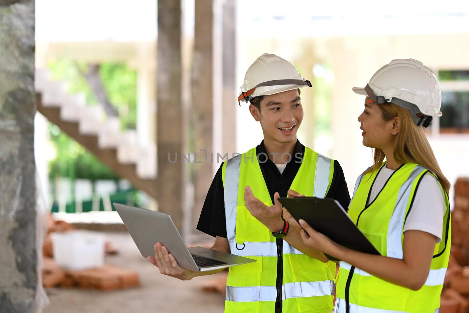 Two young engineer wearing uniform and safety helmet inspecting industrial building construction site. Industry, Engineer, construction concept.
