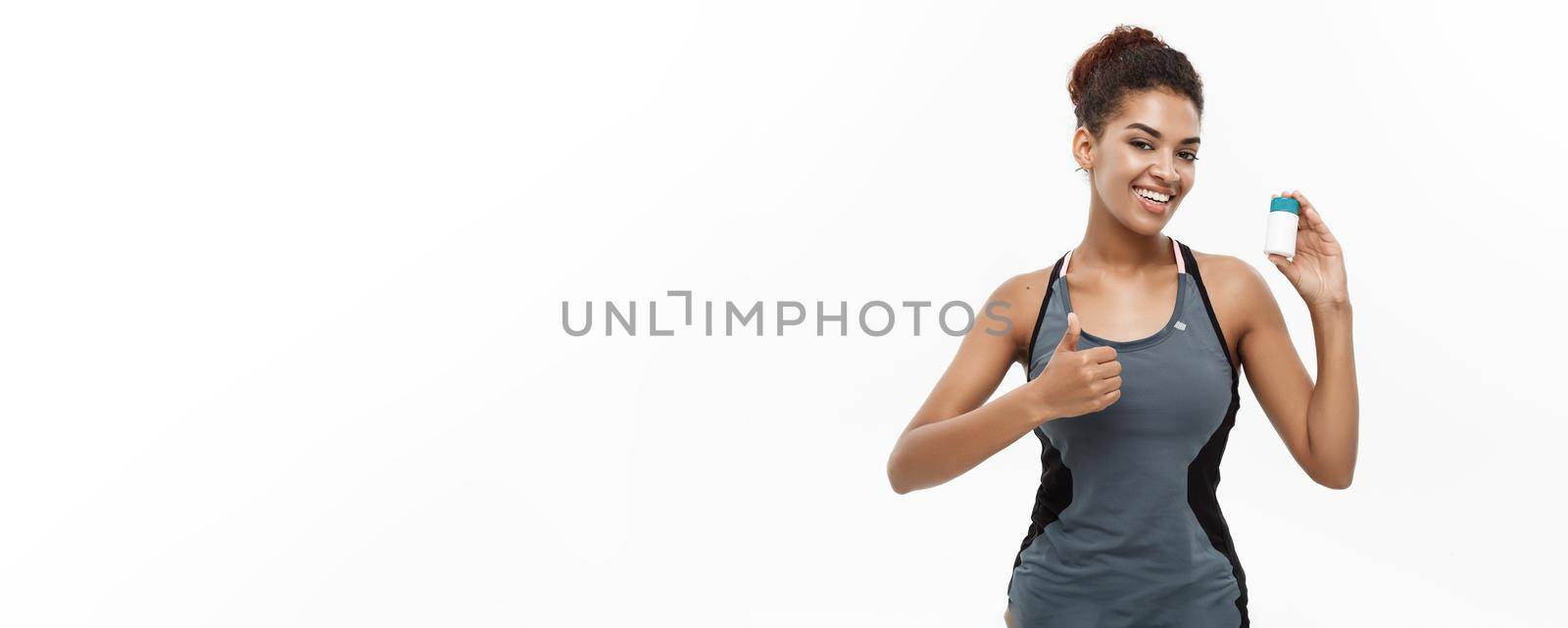 Healthy and healthcare concept - portrait of beautiful sporty African American holding bottle of supplementary bottle. Isolated on white studio background