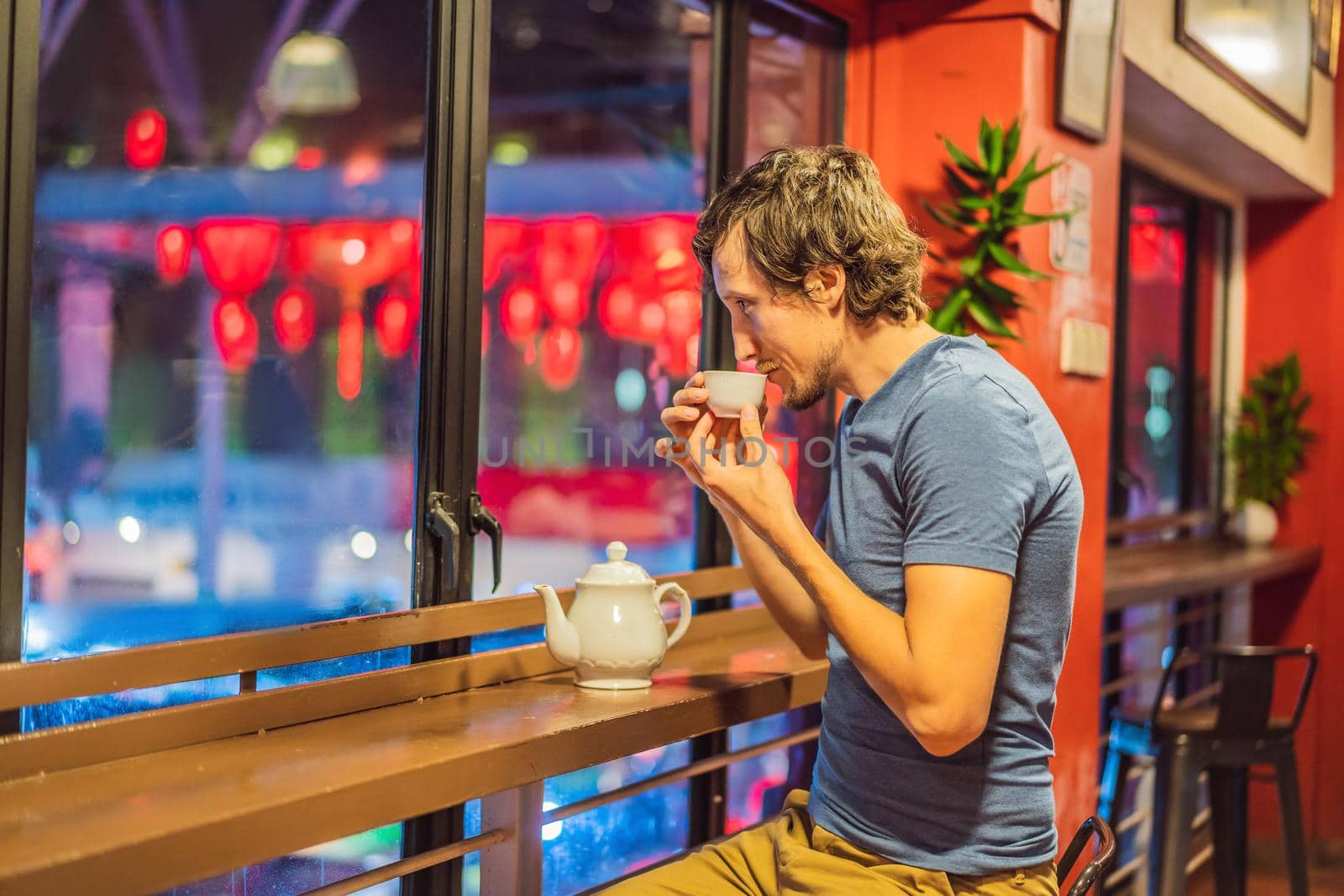 A young man drinks Chinese tea on a background of red Chinese lanterns in honor of the Chinese New Year by galitskaya