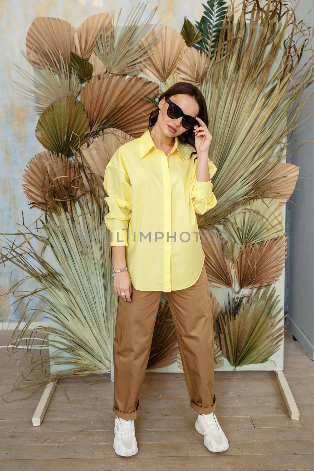 A model girl in a yellow shirt and brown sweatpants is standing in the studio. Black glasses by deandy