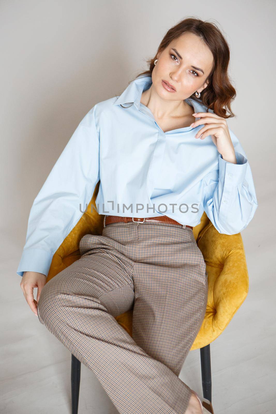 A girl in a blue shirt and trousers is sitting on a yellow chair. Shooting fashion clothes by deandy