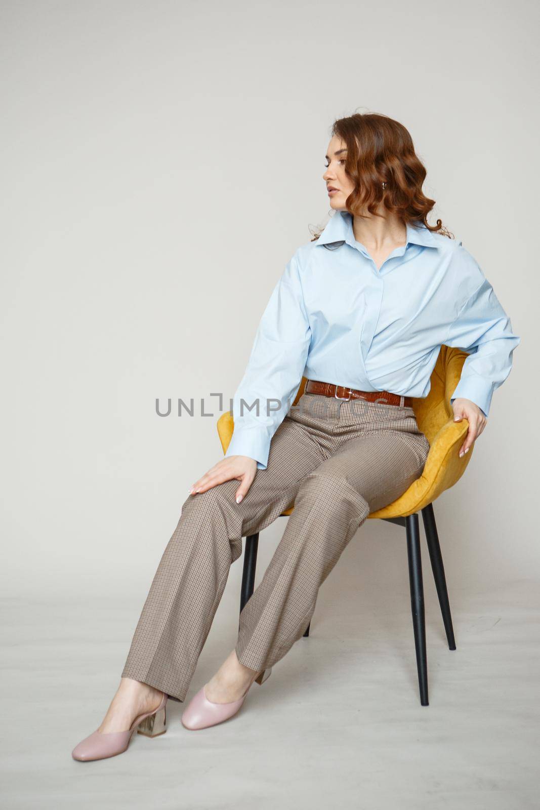 A girl in a blue shirt and trousers is sitting on a yellow chair. Shooting fashion clothes by deandy