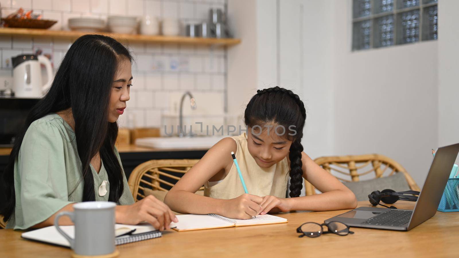 Mother helping helping daughter studying remote homeschool on computer laptop, doing homework in kitchen by prathanchorruangsak