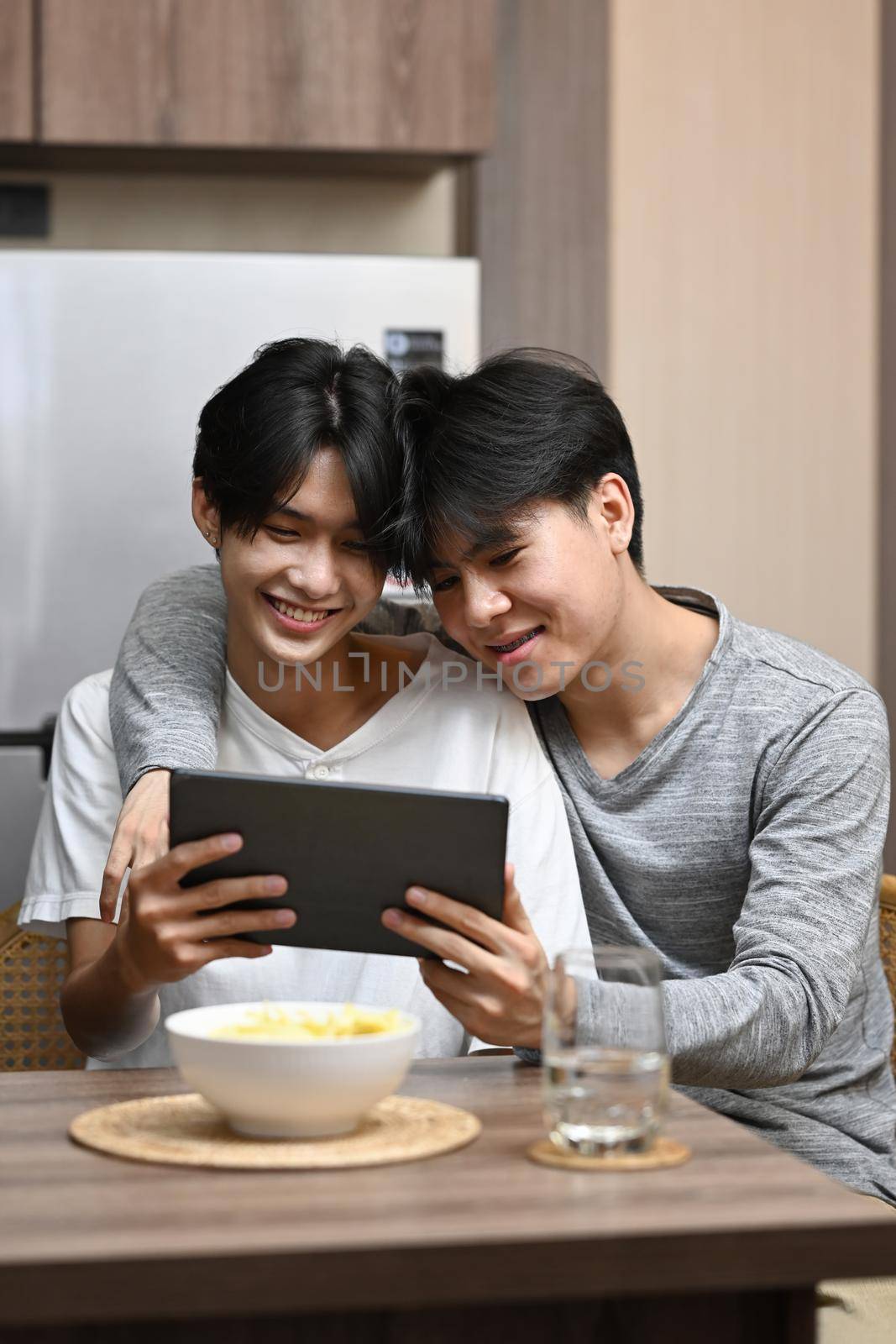 Happy LGBT couple enjoying the movie on digital tablet while spending leisure time together at home by prathanchorruangsak