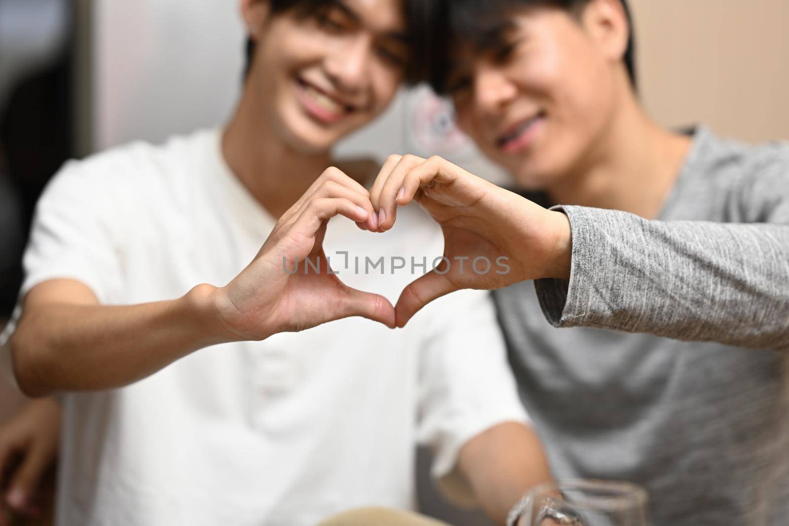 Loving homosexual couple making heart with hands and smiling to camera. LGBT, relationships and equality concept by prathanchorruangsak