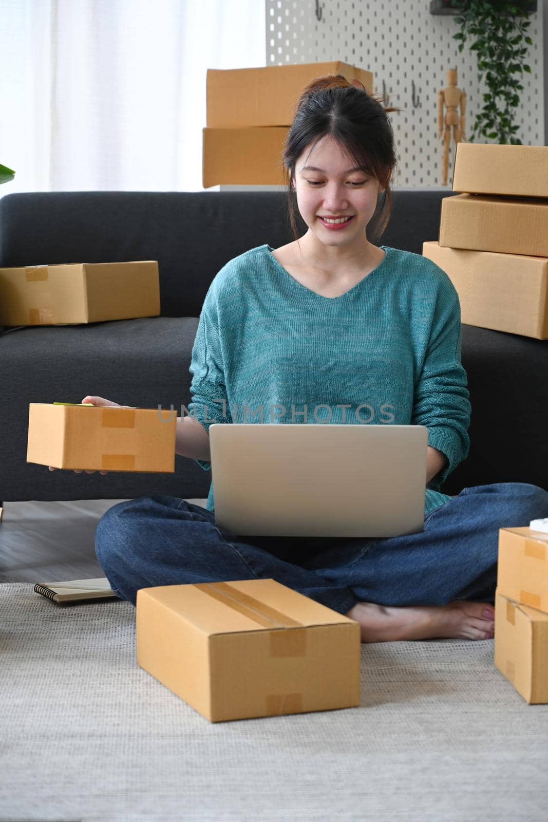 Smiling young man checking product purchase order on laptop computer and preparing parcel for delivery.