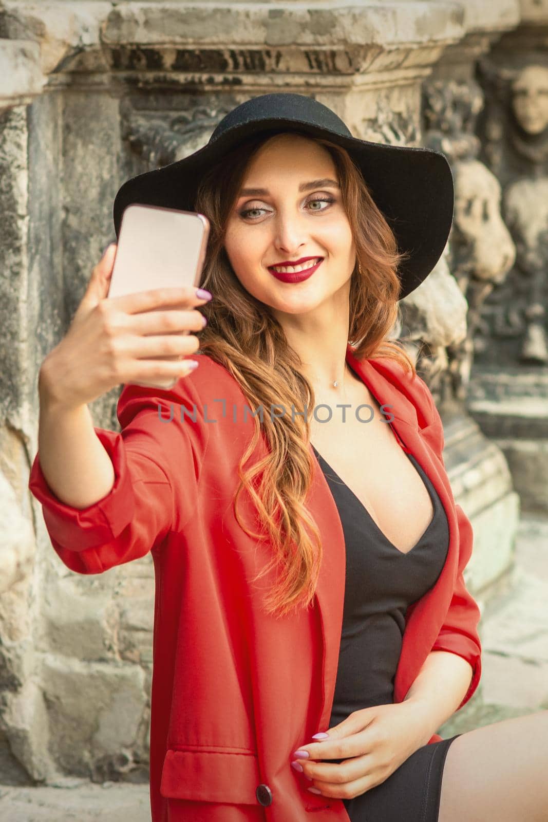 Stylish young woman is taking selfie walking on the street of old European city.