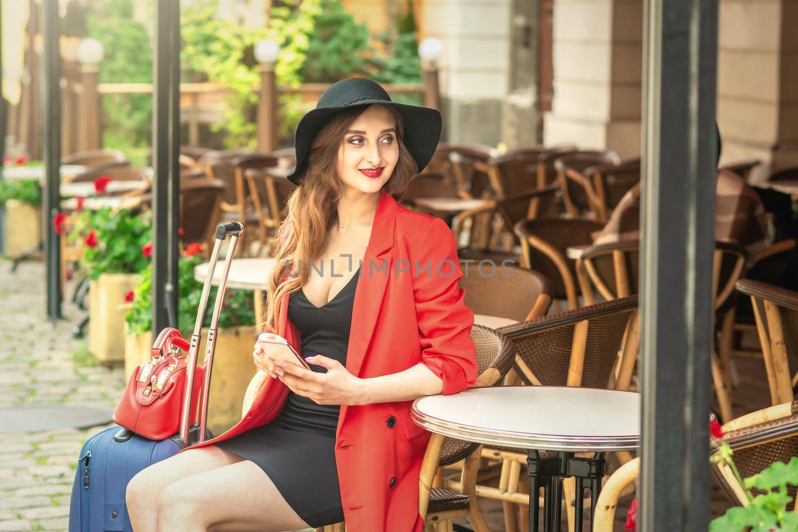 Beautiful young woman sitting in street cafe holding mobile phone outdoors.