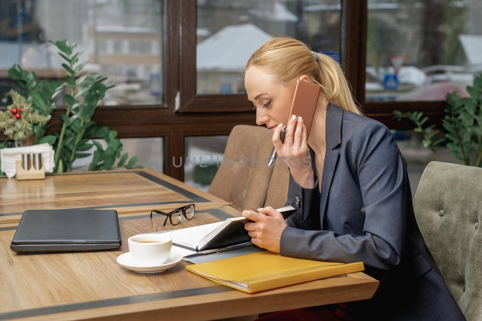 Young woman is talking by cell phone sitting at the table in home office.