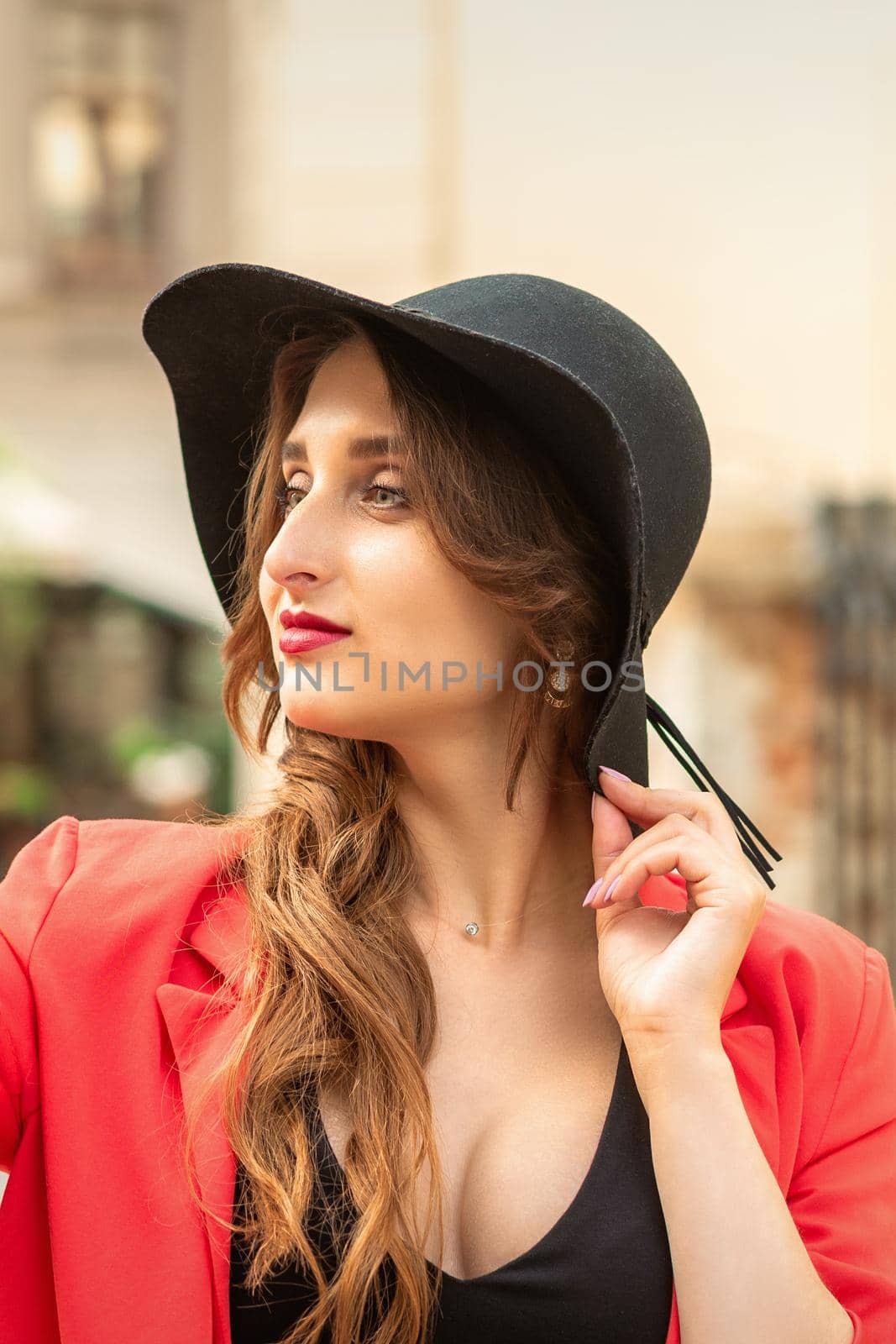 Side view of fashionable young woman in red coat and black hat looking away on the city street.