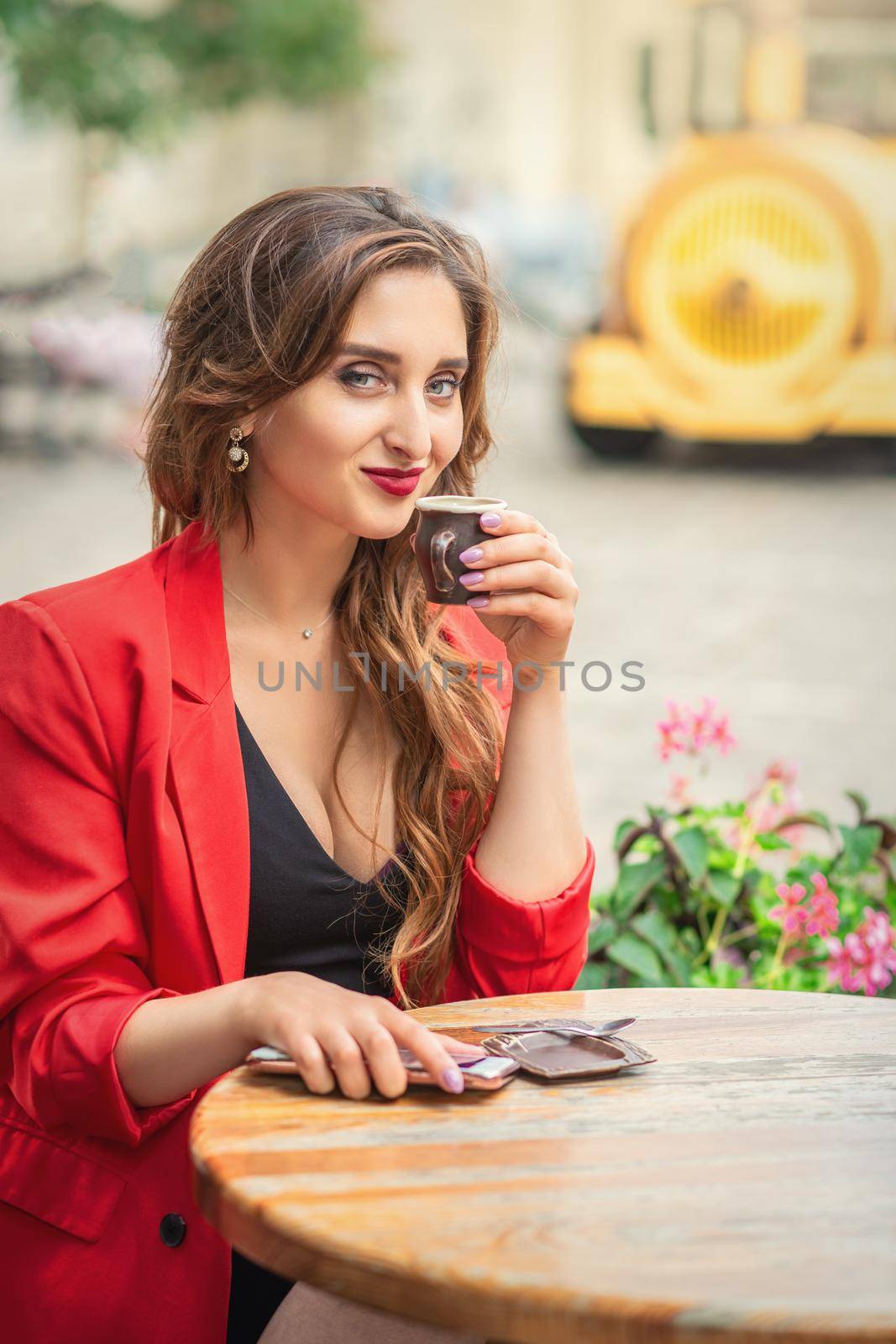 Portrait of young woman with cup drinking coffee at city street cafe.