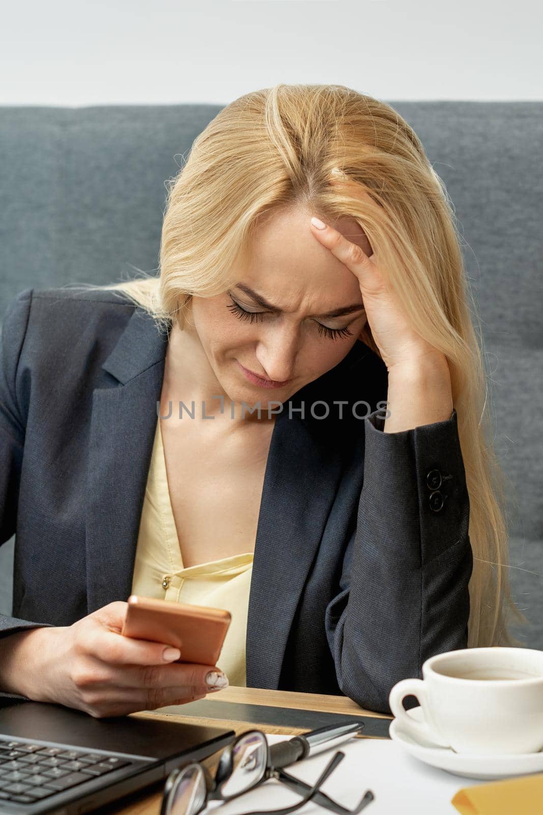 Young female office worker looking at cell phone screen looks surprised dissatisfied at home office.