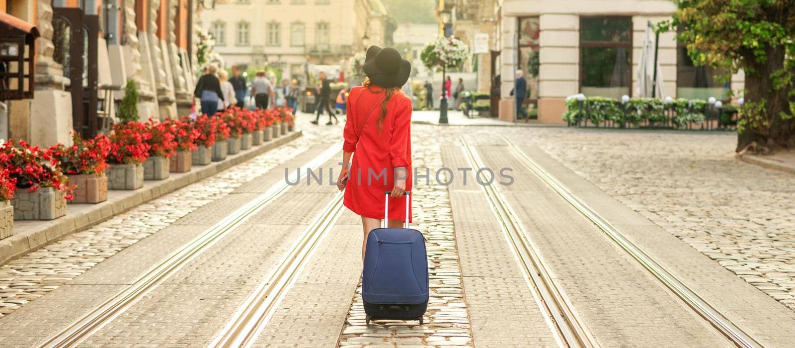 Beautiful young girl is walking with blue suitcase on the tram track road of the street of old European city.