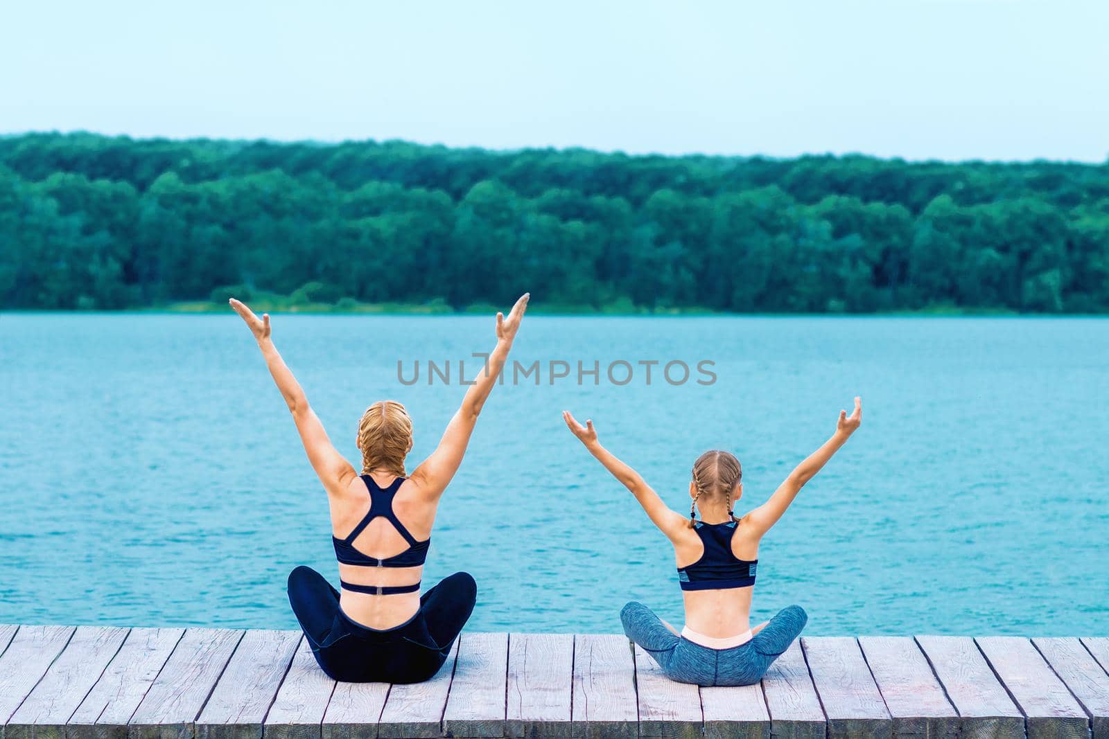 Mother and daughter doing yoga at the shore by okskukuruza