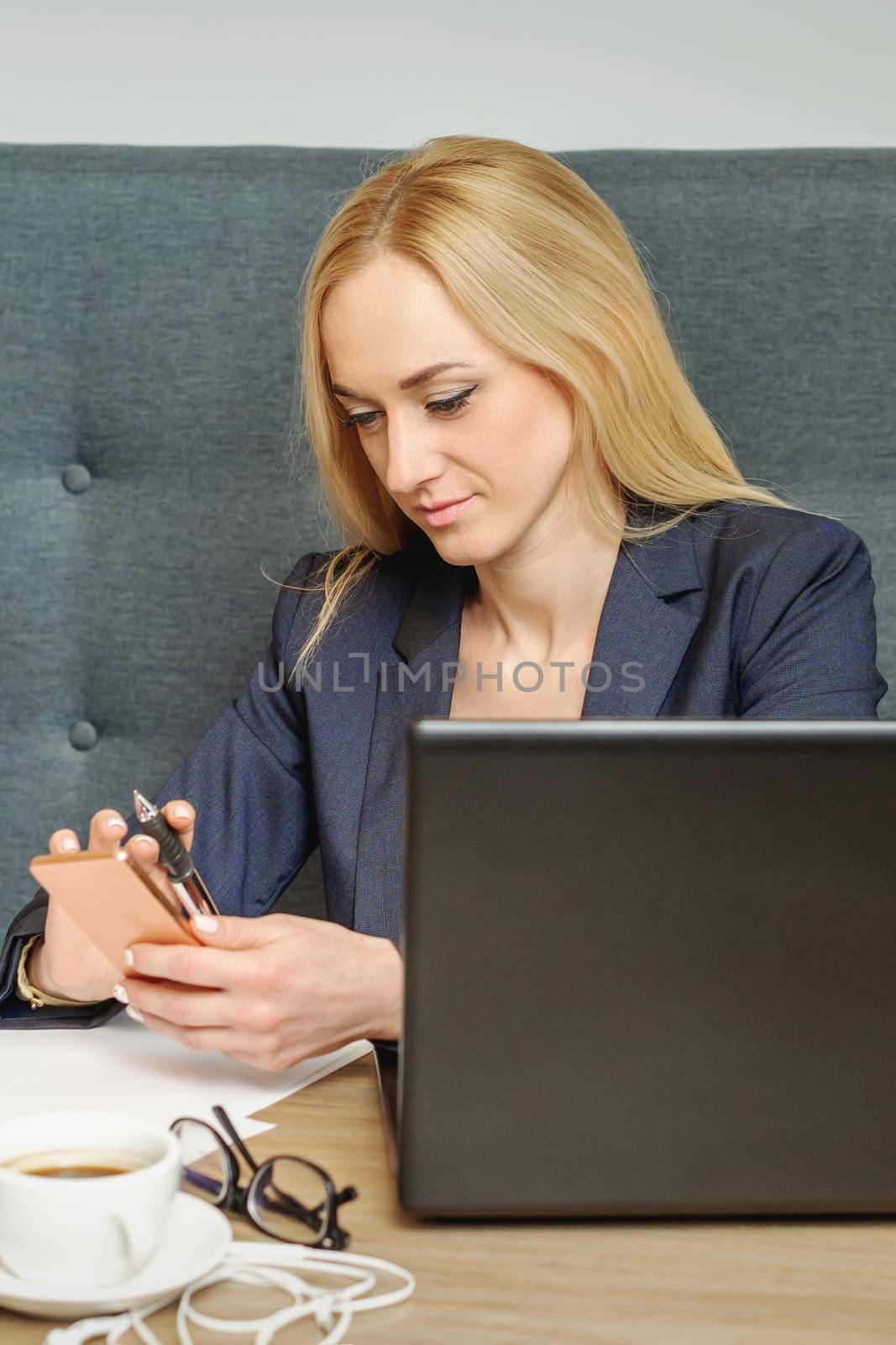 Business woman texting on the phone and working on laptop sitting on workplace.