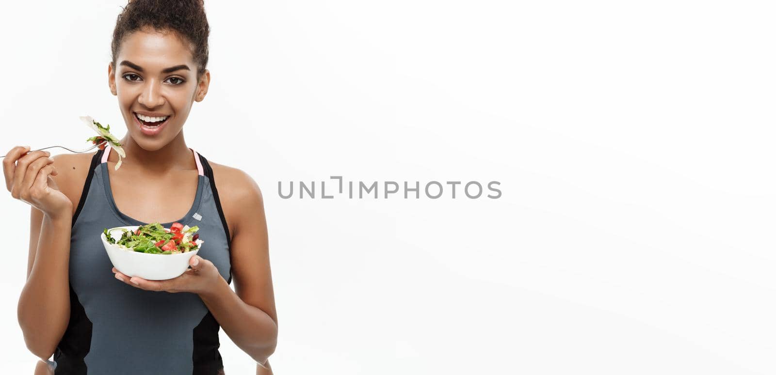 Healthy and Fitness concept - Beautiful American African lady in fitness clothes on diet eating fresh salad. Isolated on white background