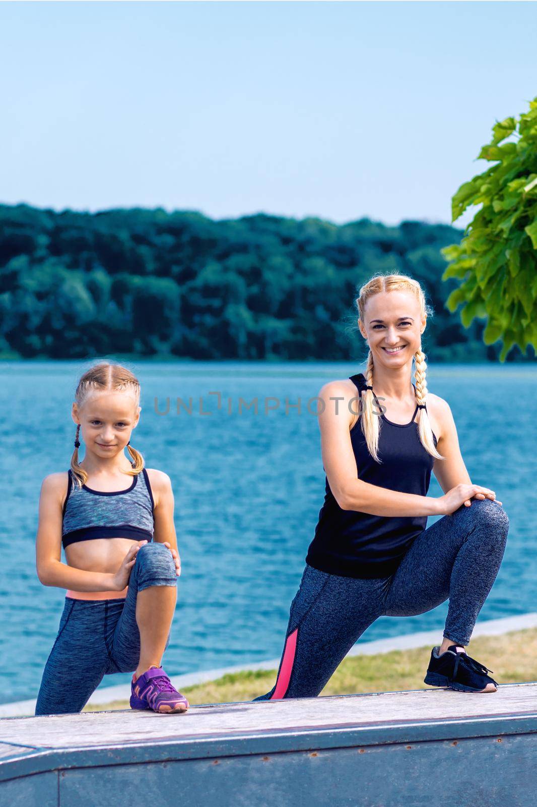 Portrait of mother and child in sport style clothes on the shore of the lake.