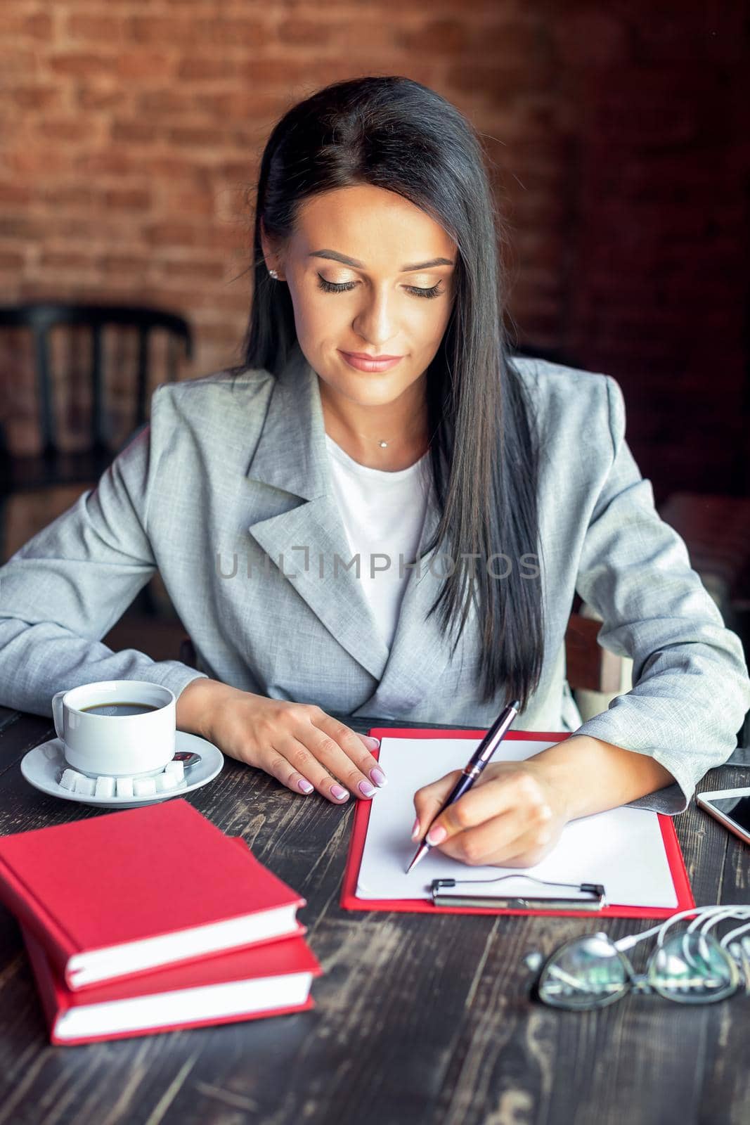 Beautiful young business woman is writing on white paper in the cafe.