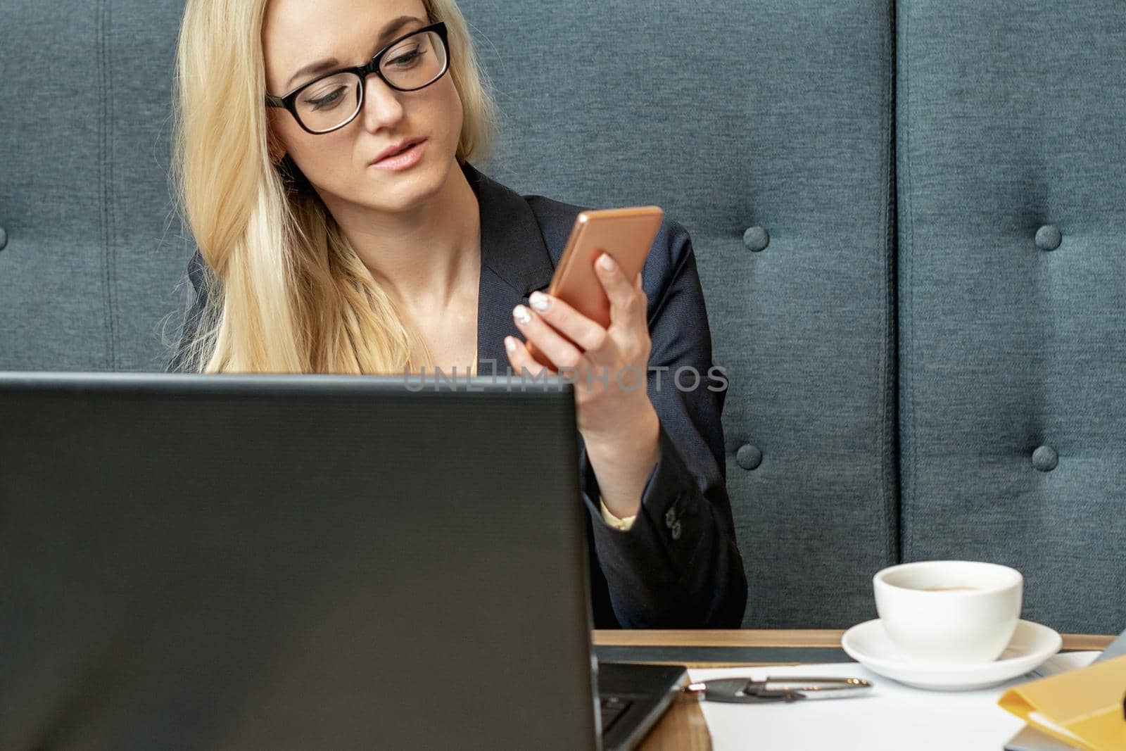 Beautiful woman holding a smartphone in hand while sitting at the wooden working table in home office.