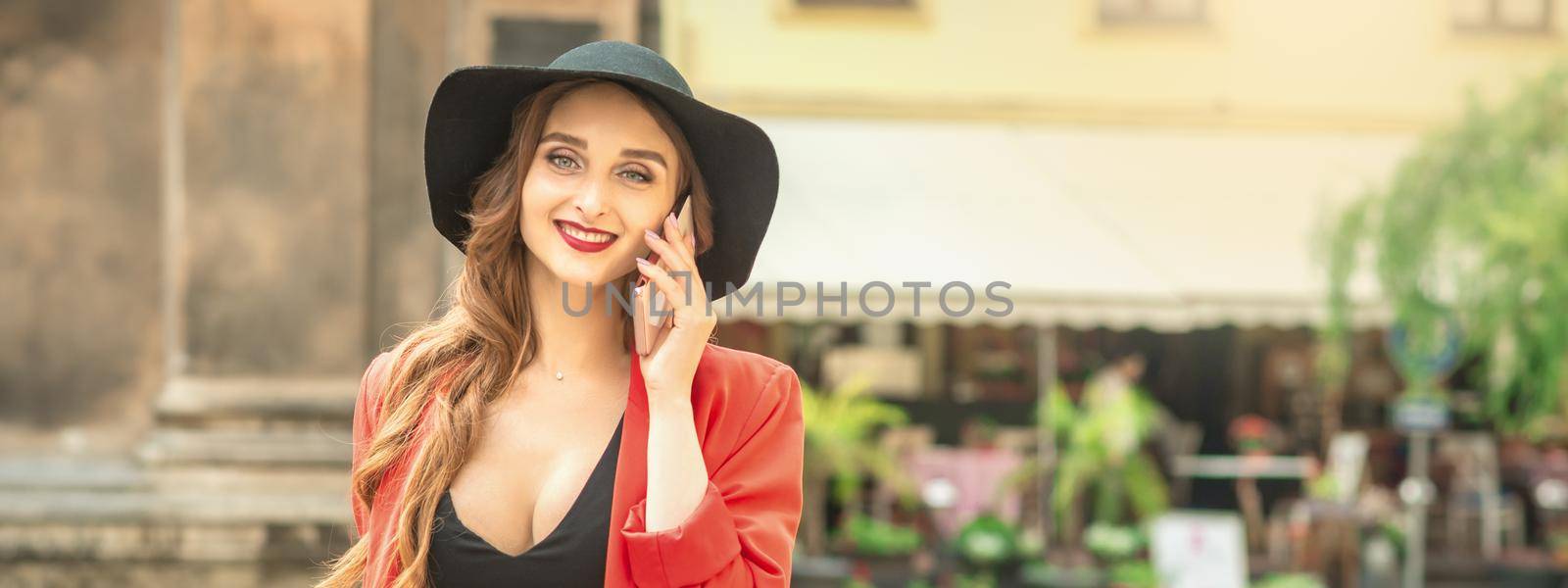 Long haired lady in fashionable black hat calling by mobile phone on the street of old city.