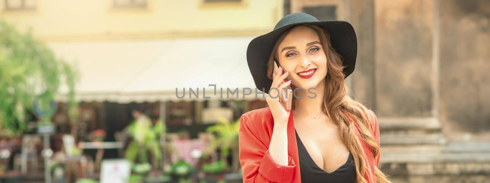 Portrait of young smiling fashionable girl talking by phone wearing black hat outdoors on the city street.