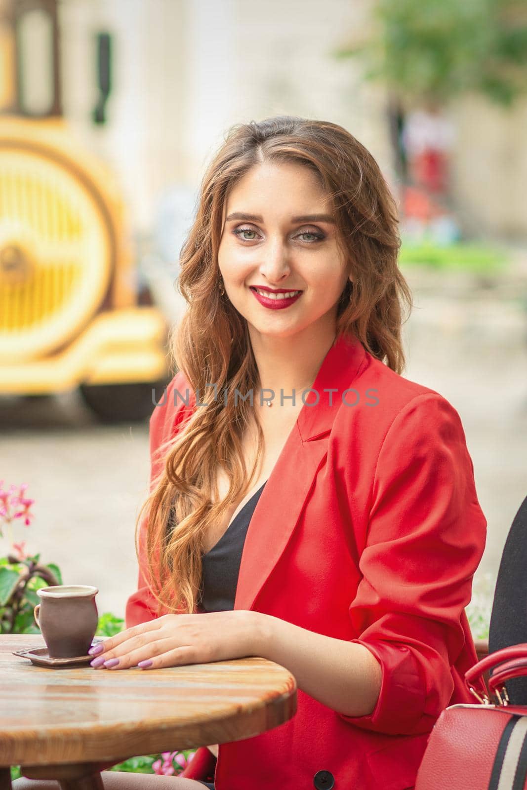 Outdoor portrait of pretty woman having cup of coffee at cafe table on the city street.