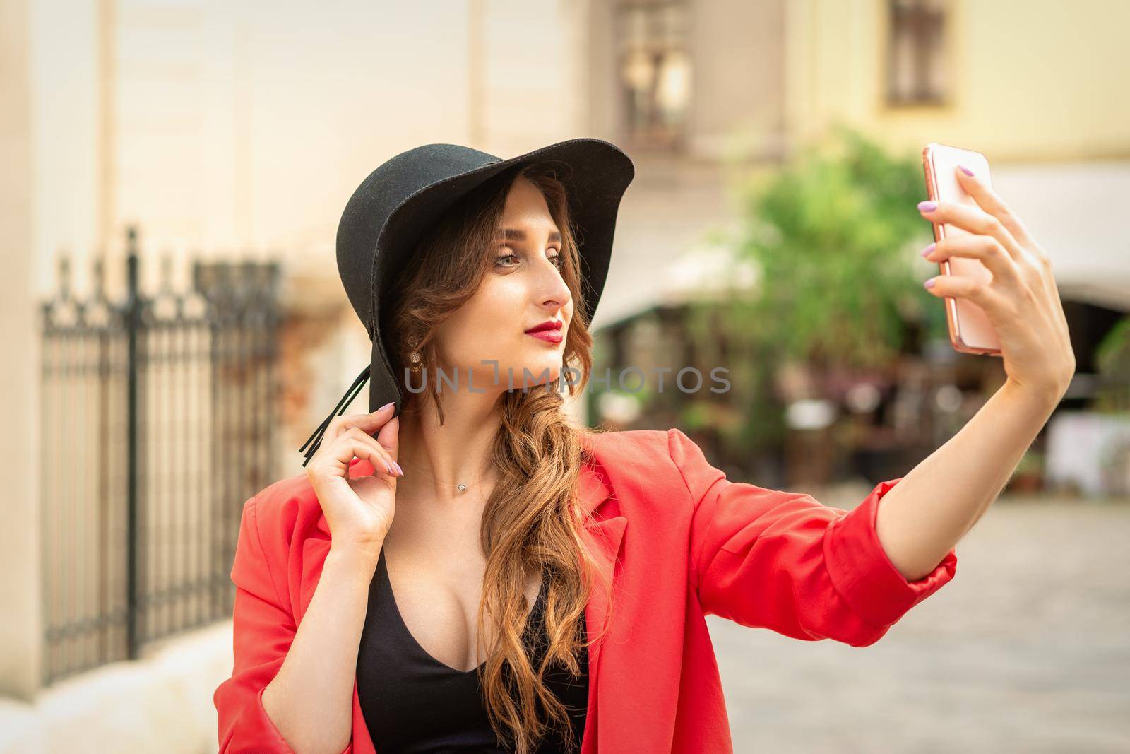 Happy young lady is taking photo of herself by smartphone on the city street.