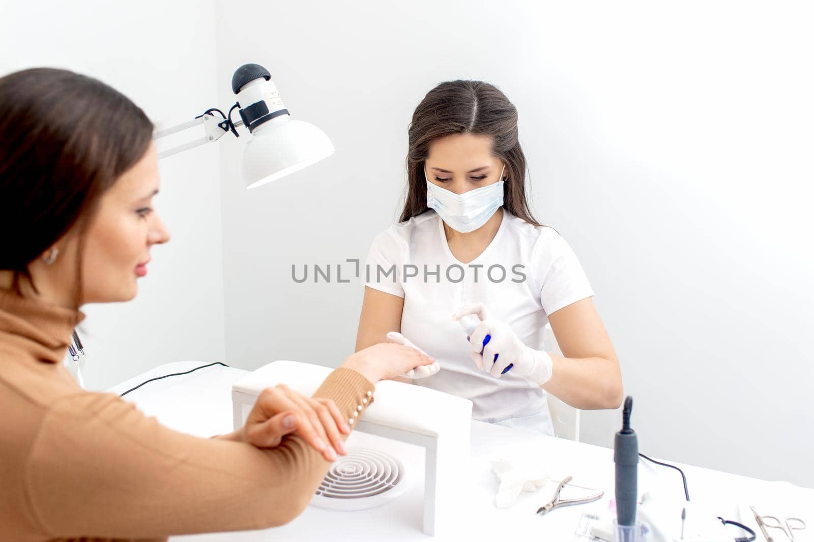 Manicurist is applying antiseptic on client's hands in manicure salon.